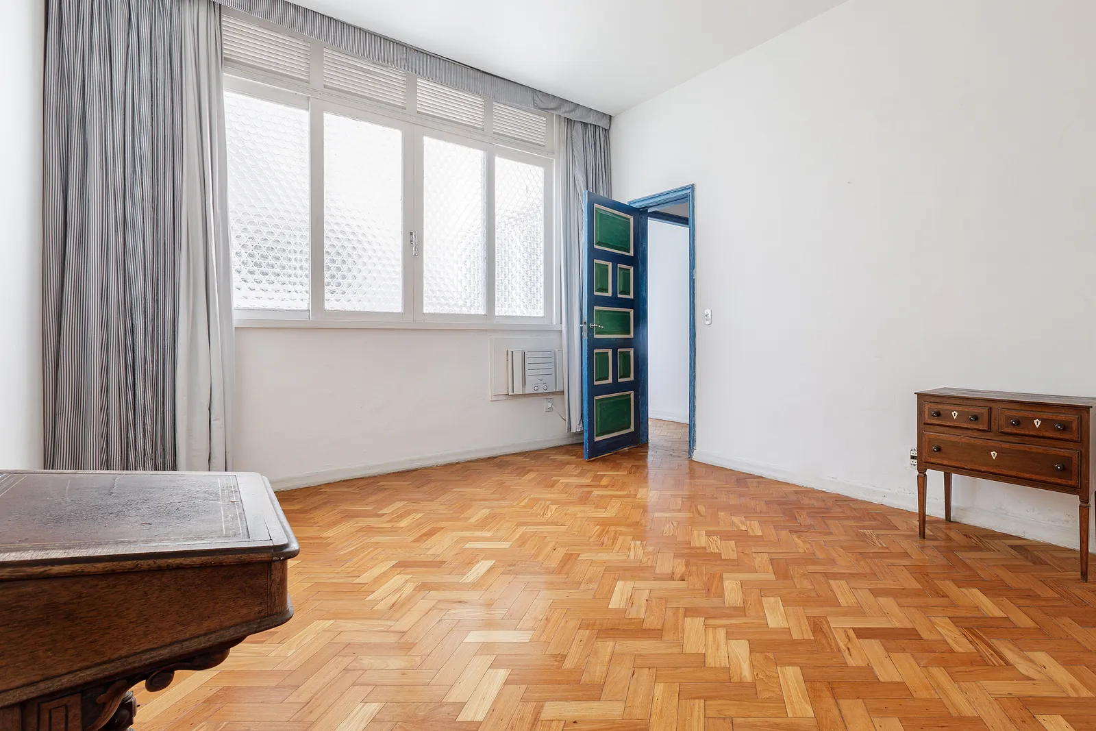 A bedroom with a full window wall and patterned curtain