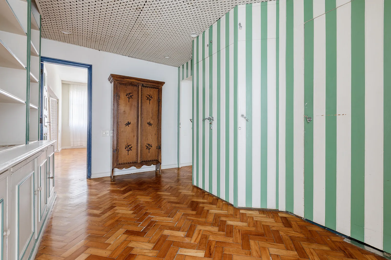 A bedroom with a green striped wall and a wooden armoire