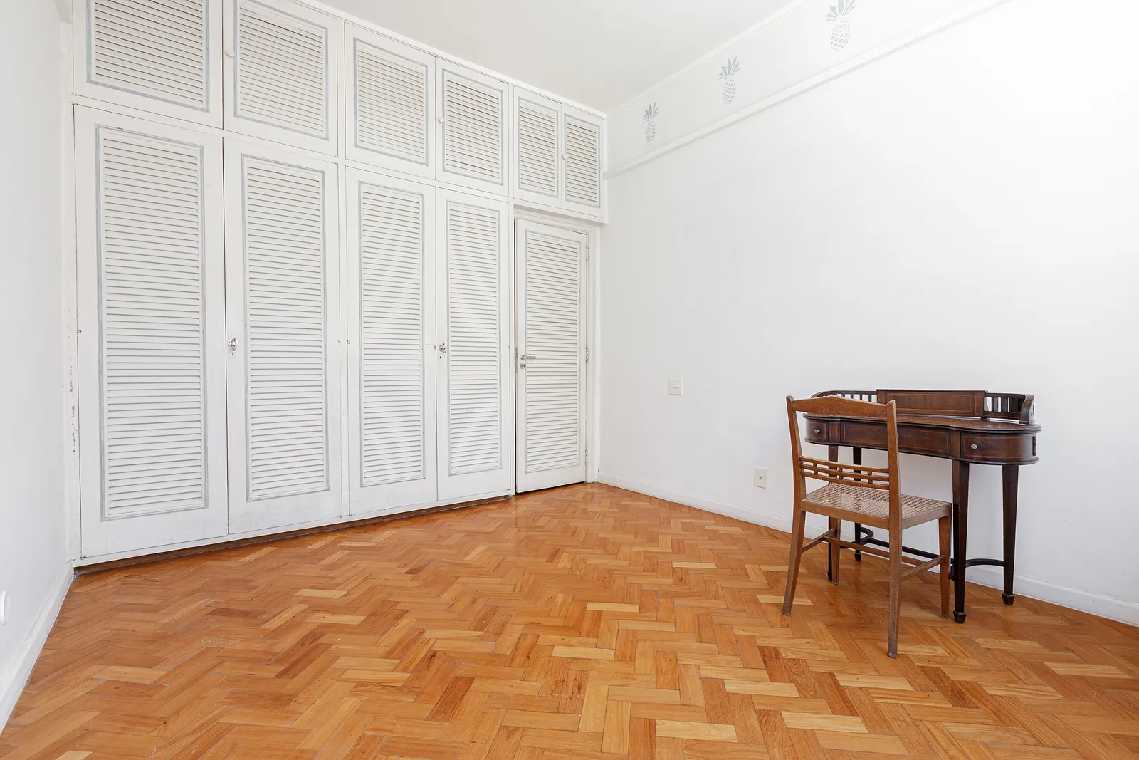 A bedroom with carved white wardrobes and parquet