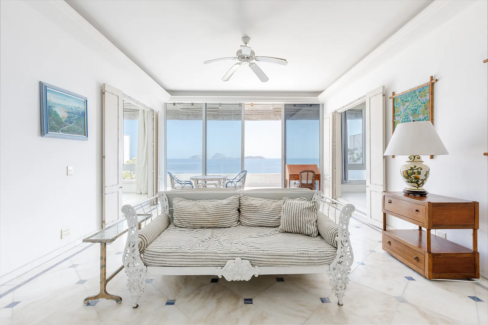 A living room with wide windows onto the sea, white sofas