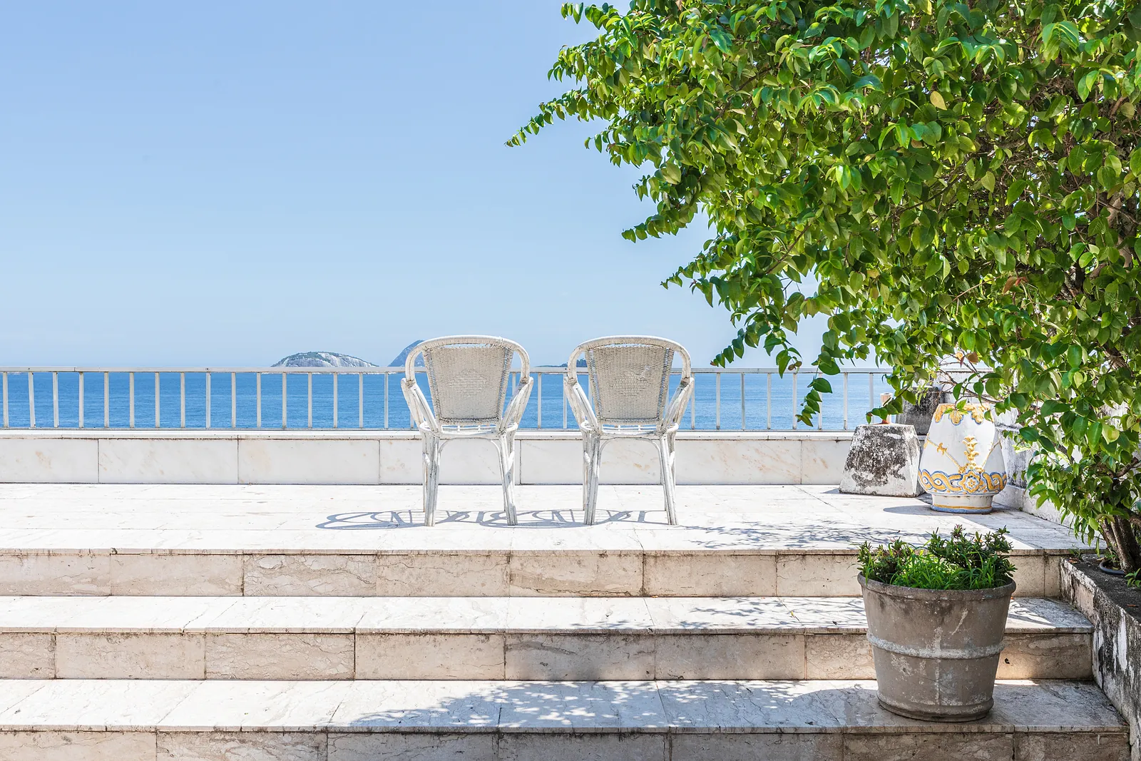 A rooftop terrace with a tree, chairs and the sea beyond
